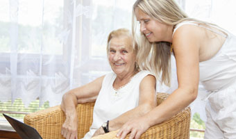woman leaning over other woman in chair, both smiling