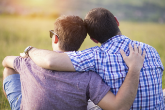 backs of 2 men sitting outside with their arms around each other